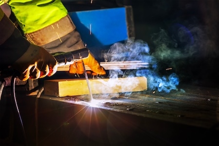 Welder using a SMAW torch with consumable stick welding electrodes.